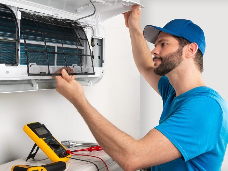 Installation service fix  repair maintenance of an air conditioner indoor unit, by cryogenist technican worker checking the air filter in blue shirt and baseball cap